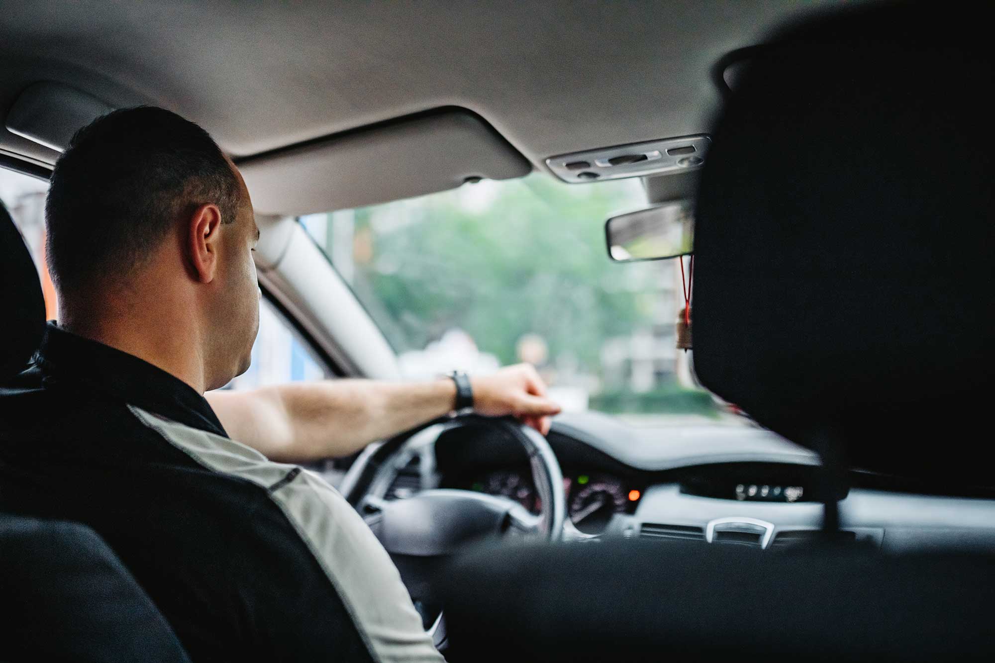 En man kör bil genom stadsgator en solig dag