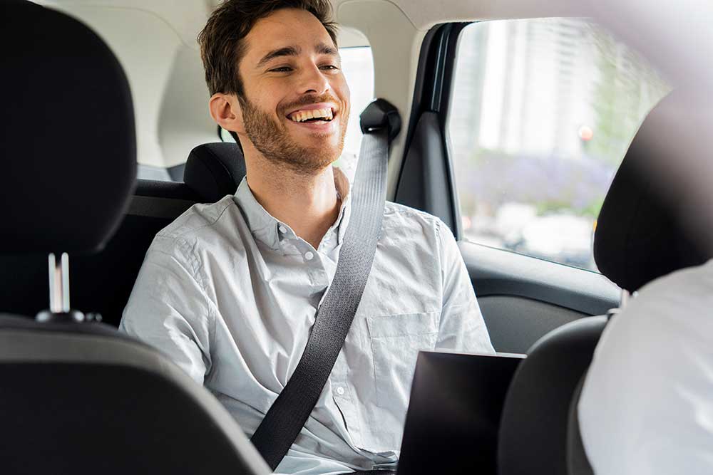 En glad ung man i ljusblå skjorta sitter bekvämt på passagerarsätet i en taxi